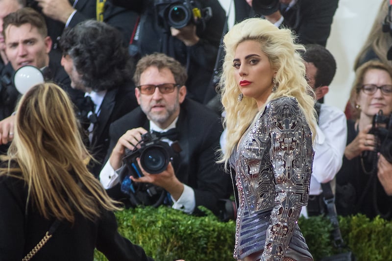 Lady Gaga is posing on the red carpet in a beaded gown with red lipstick