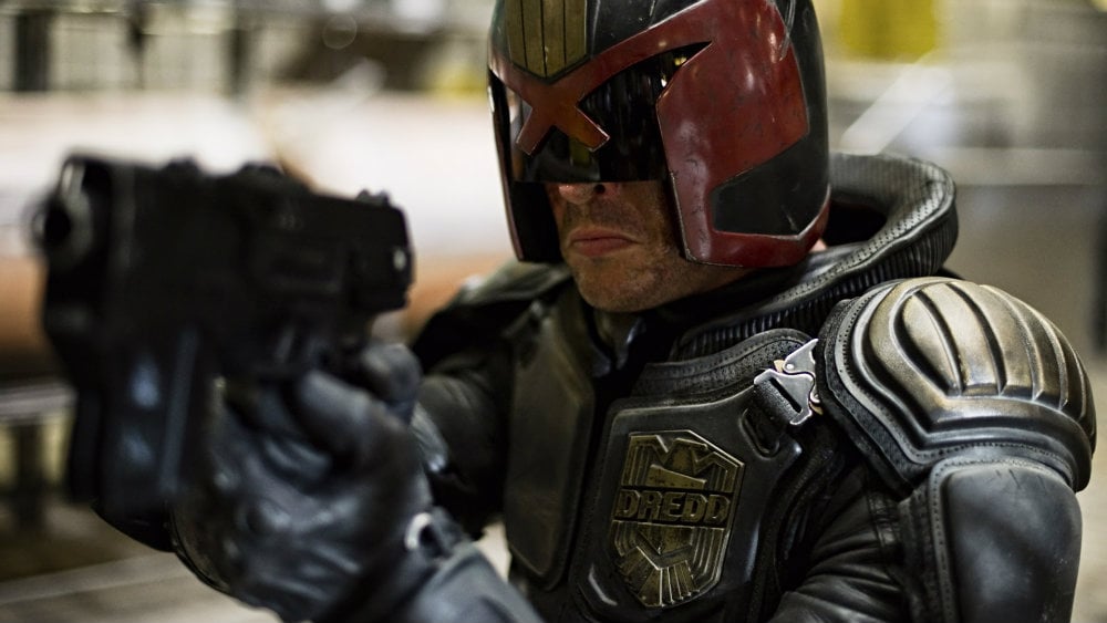 Karl Urban in Dredd holds a gun while in his suit and mask