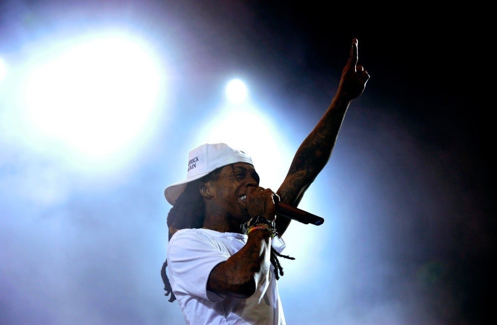 Lil Wayne wearing a white hat and shirt, rapping into a microphone