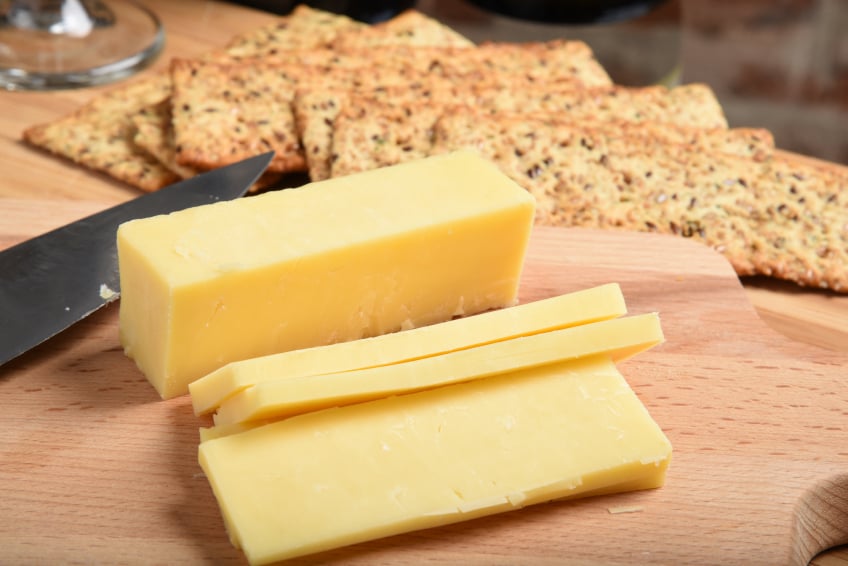 slicing white cheddar cheese ona cutting board with a knife