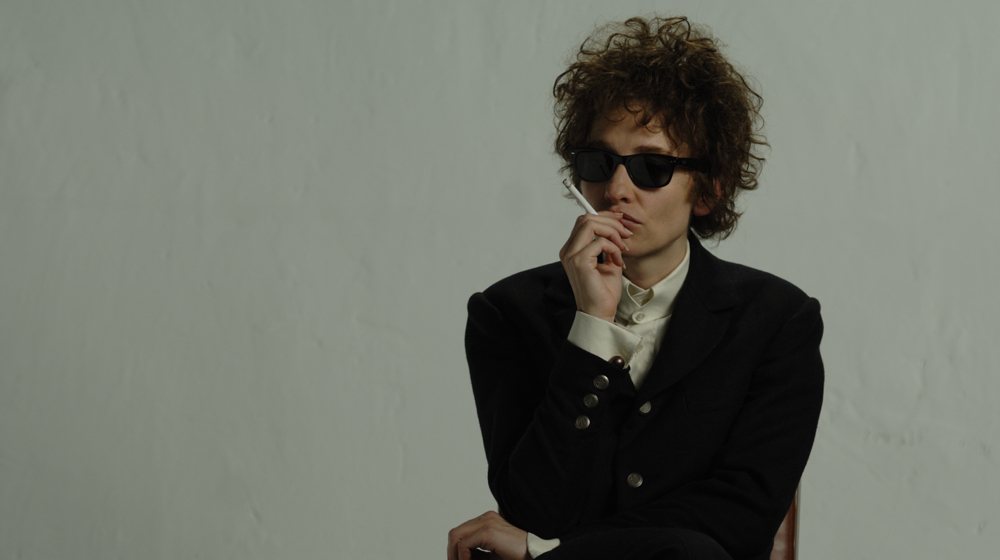 Cate Blanchett dressed as Bob Dylan, smoking a cigarette in sunglasses