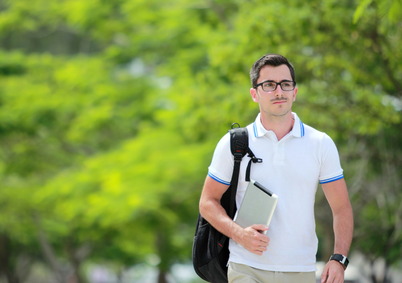 young man walking outside with a backpack over one shoulder