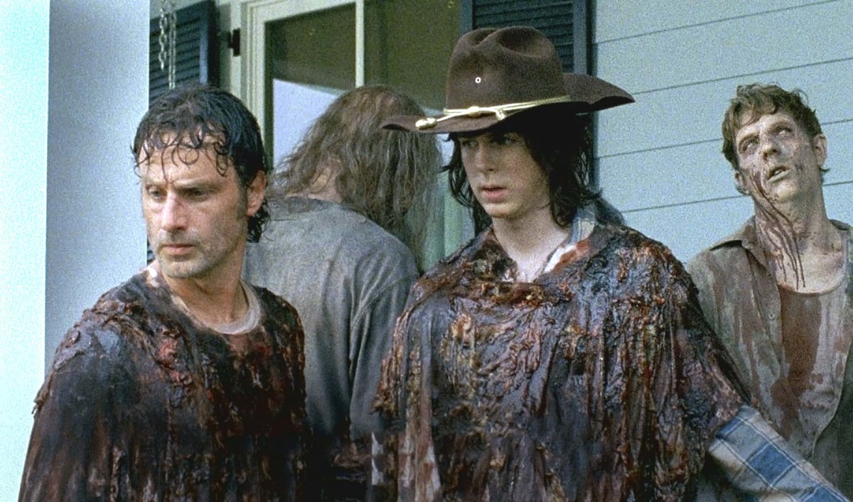Rick (Andrew Lincoln) and Carl (Chandler Riggs) walk through Alexander wearing zombie guts in a scene from 'The Walking Dead's sixth season.