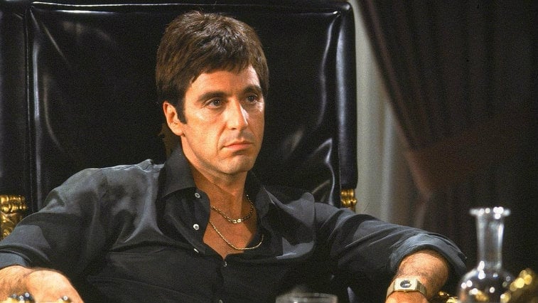 Al Pacino in Scarface sitting in a large leather chair.