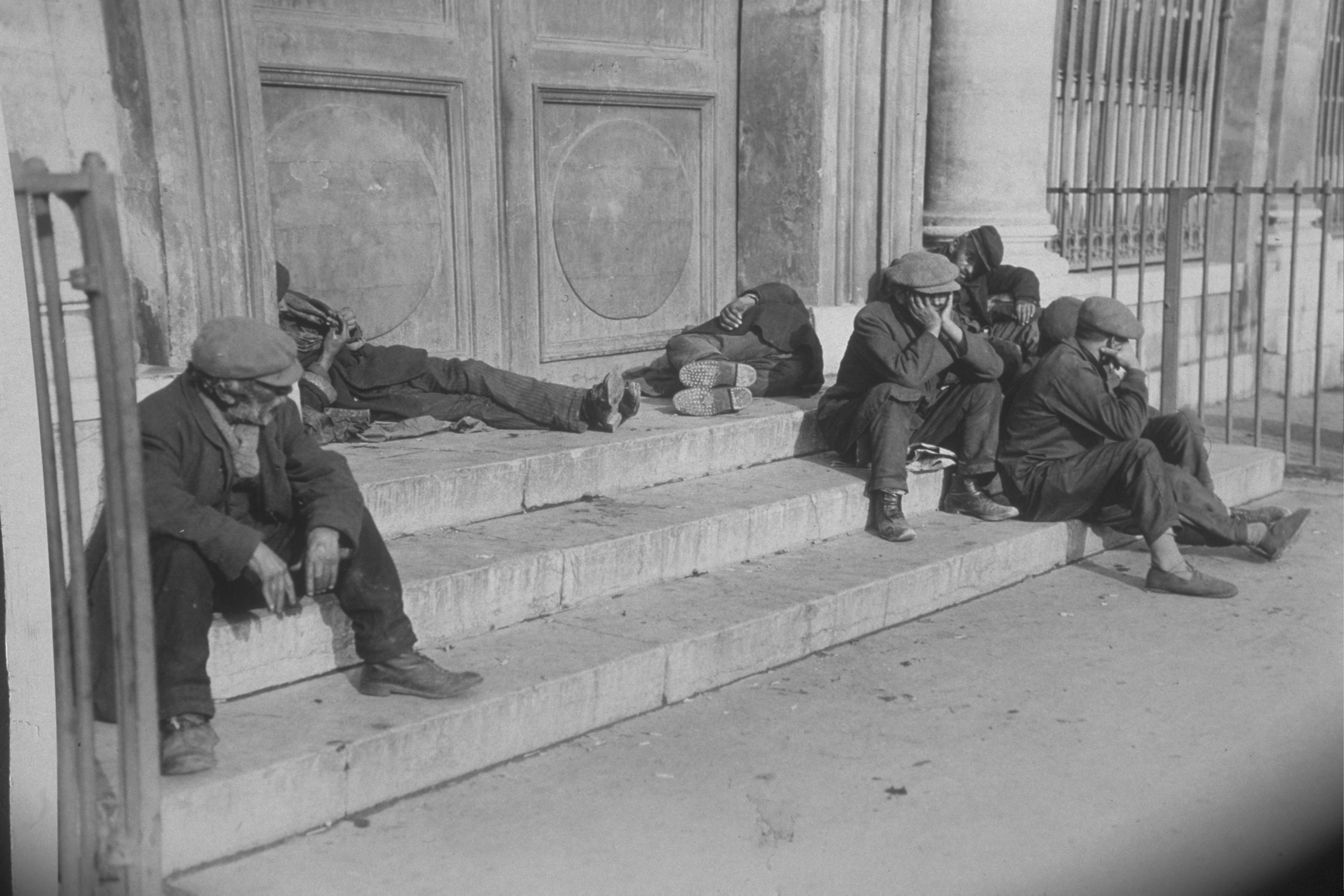 Beggars, suffering from a lack of affordable housing, on the steps of a town hall 