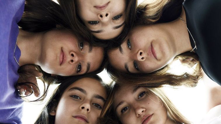 Five girls with their heads together and solemn expressions