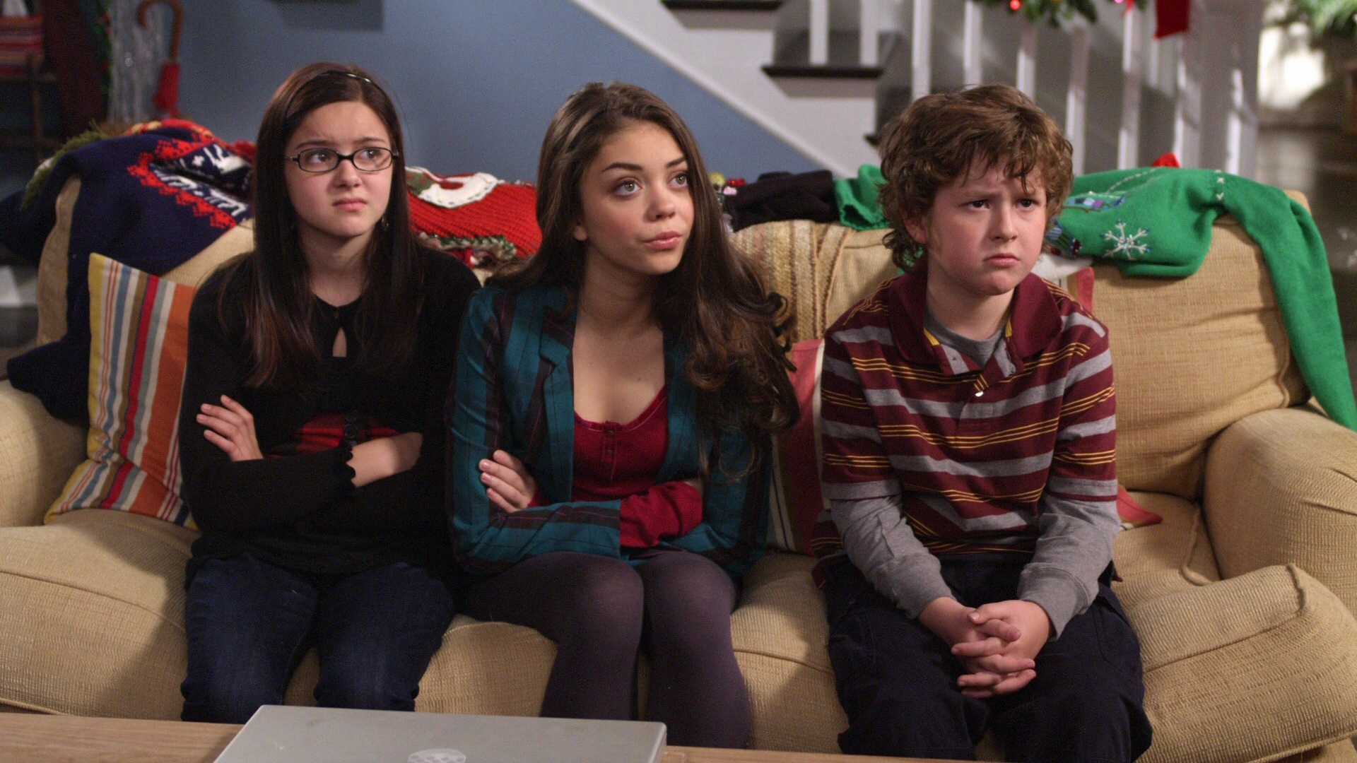 Sarah Hyland, Ariel Winter,and Nolan Gould sit on a couch and stare ahead in Modern Family
