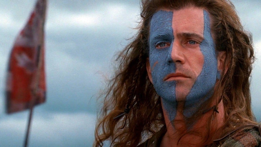 Mel Gibson with blue paint in parts of his face in front of a flag