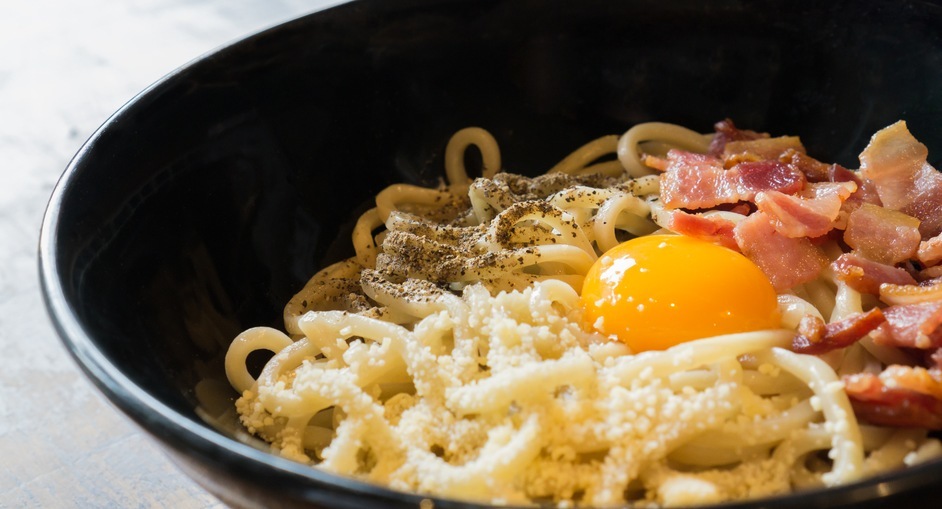 close-up of a bowl filled with noodles, bacon, and an egg
