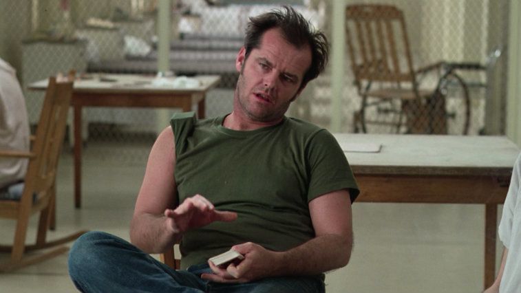 Jack Nicholson sitting in a chair with cards in his hand in One Flew Over the Cuckoo's Nest