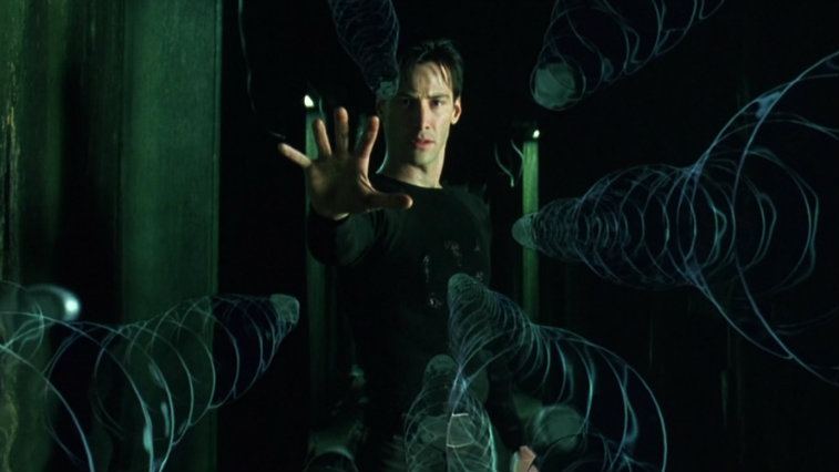 Keanu Reeves has his hand up to stop bullets mid-air in The Matrix