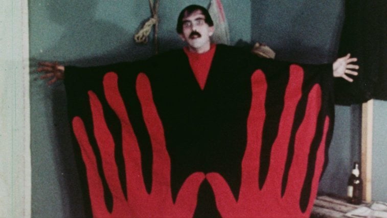 Man in a black and red outfit with giant hands printed on it from Manos: The Hands of Fate