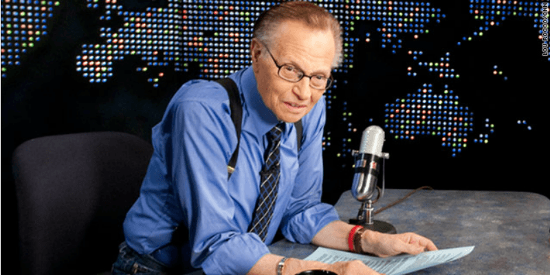 Larry King sits at his desk on his show in a blue shirt and tie