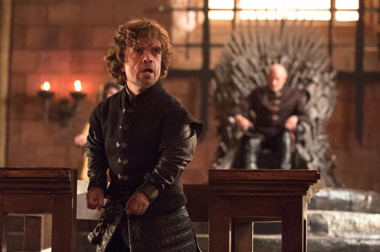 Tyrion Lannister on Game of Thrones Season 4 with a man in the background on a throne