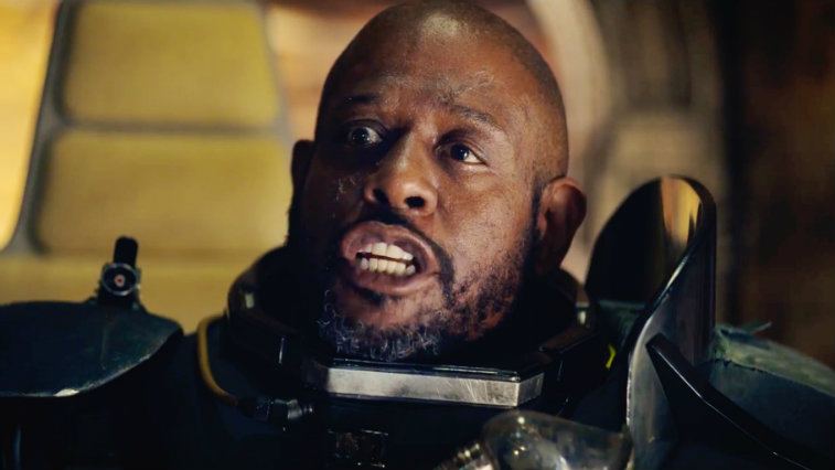 Saw Gerrera, wearing a black armored suit, and bearing his teeth