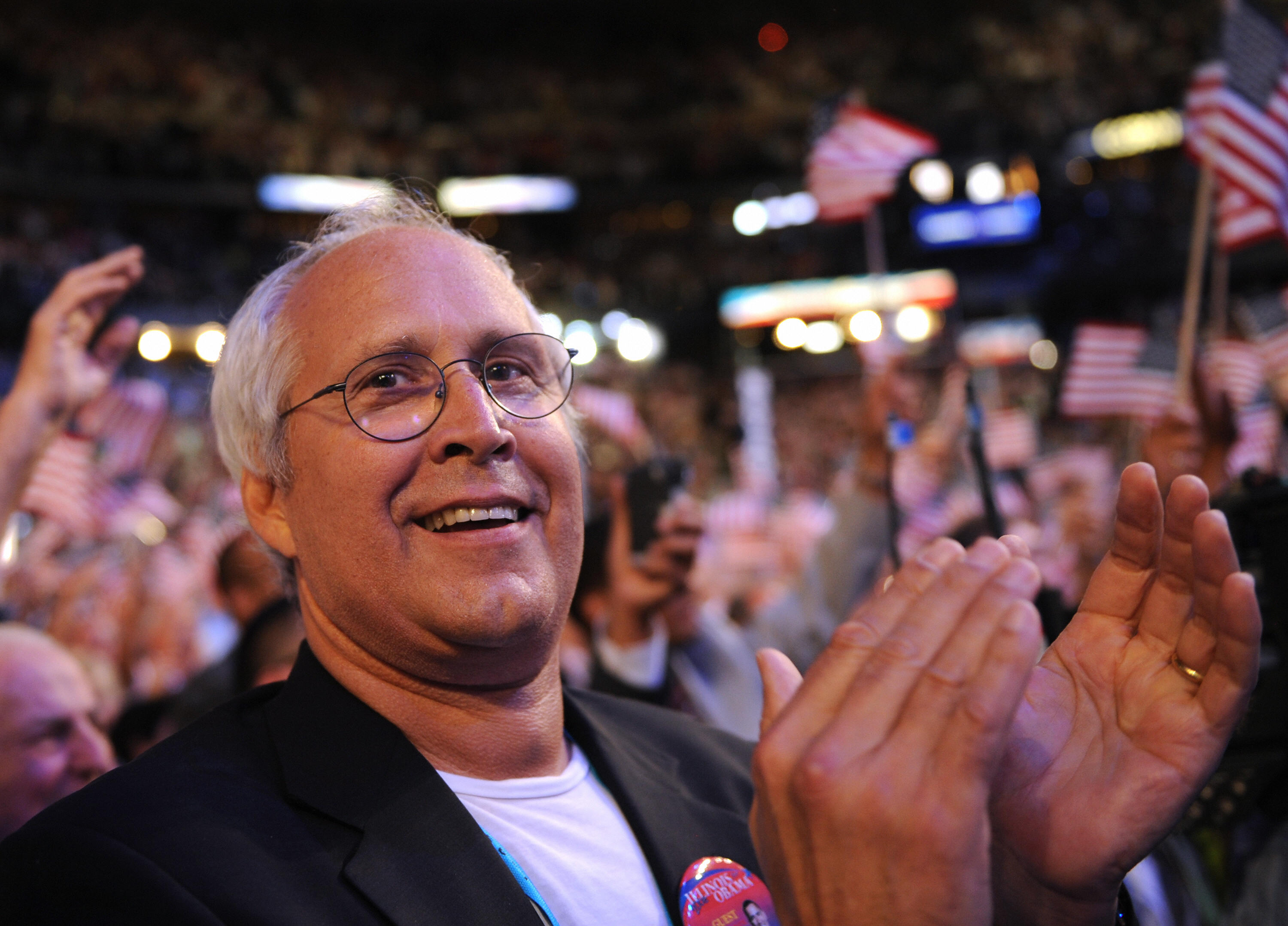 Chevy Chase stands and claps at a rally
