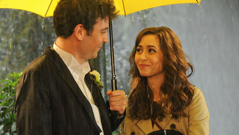 Josh Radner and Cristin Milioti standing under a yellow umbrella in the rain in How I Met Your Mother