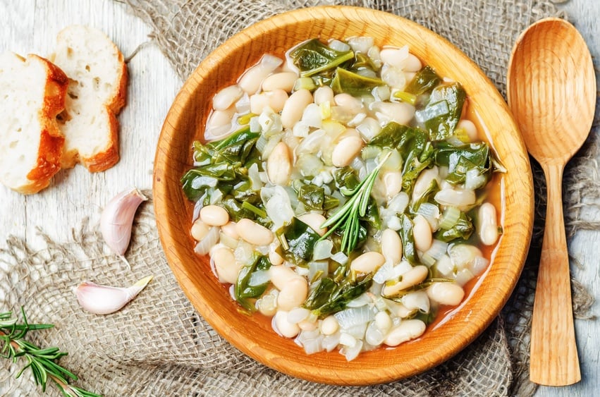 white bean spinach soup in a wooden plate with wooden spoon
