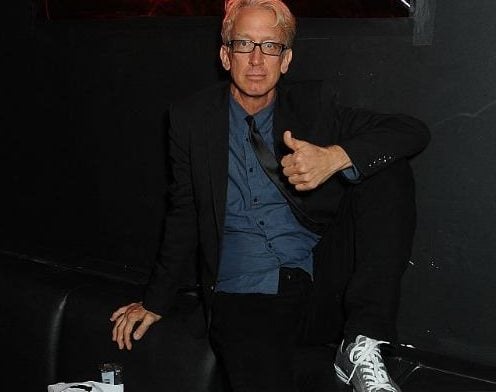 Andy Dick is sitting on a couch and giving a thumbs up.