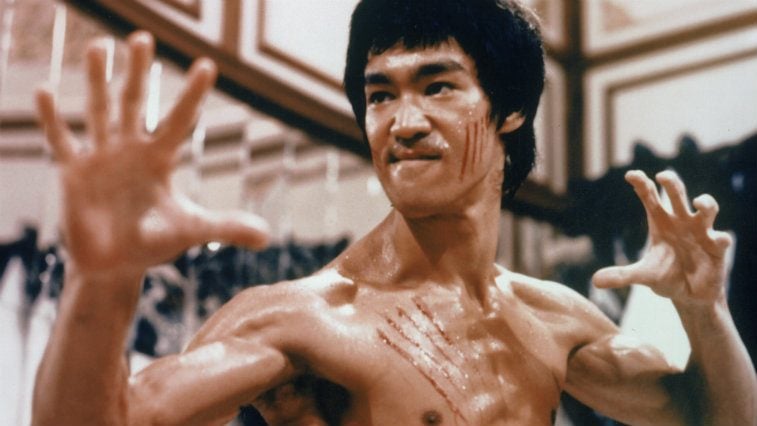 Bruce Lee with his hands out, shirtless, and ready to fight