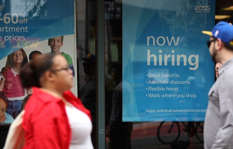 A 'now hiring' sign is posted outside of a store, advertising opportunities for employment