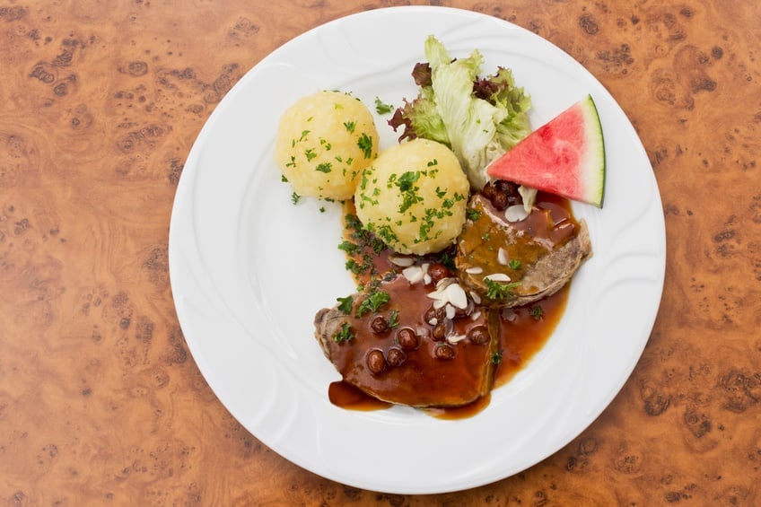 Marinated beef on a plate with potatoes, lettuce, and watermelon