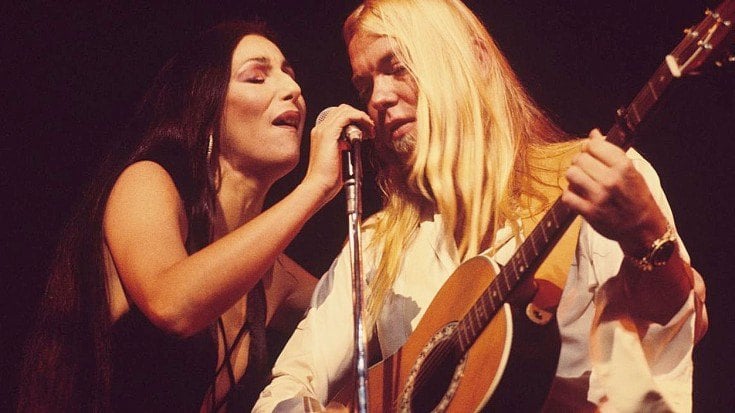 Cher and Gregg Allman singing together in front of a microphone on-stage