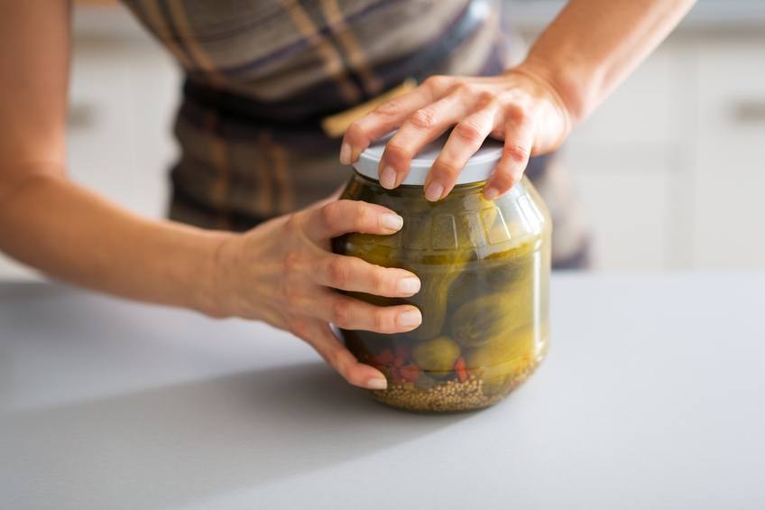 Woman trying to open a jar of pickles.