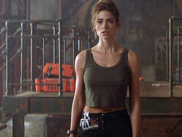 Denise Richards with her hair pulled back looking surprised in a warehouse in 'The World Is Not Enough'