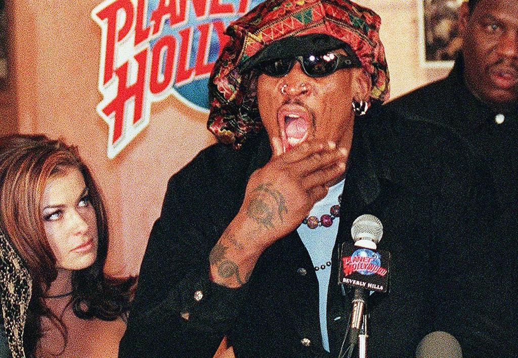 Dennis Rodman at a press conference with his mouth open, standing to the left of Carmen Electra