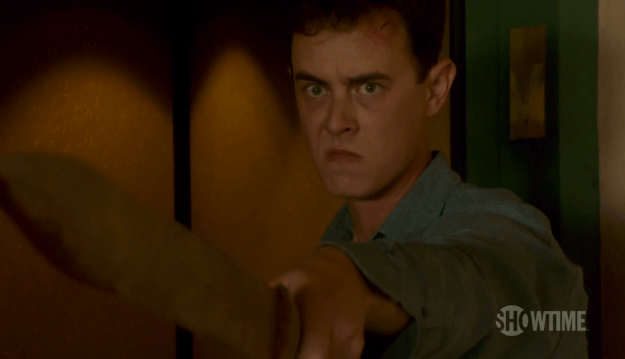Colin Hanks looks angry holding a wooden sword out in front of him on Dexter 