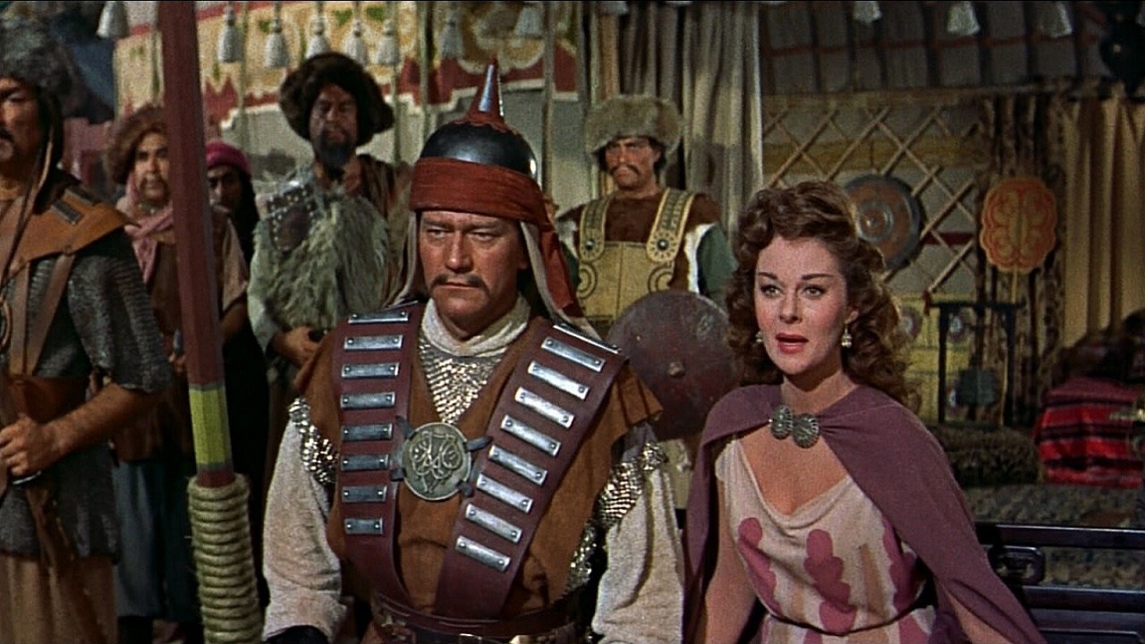 John Wayne as Genghis Khan in ancient military garb standing next to Susan Hayward as Bortai in The Conqueror