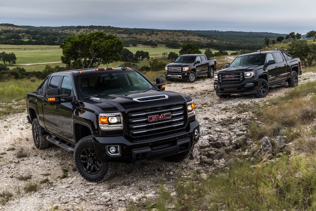 Three black GMC pick-up trucks parked on a rocky road.