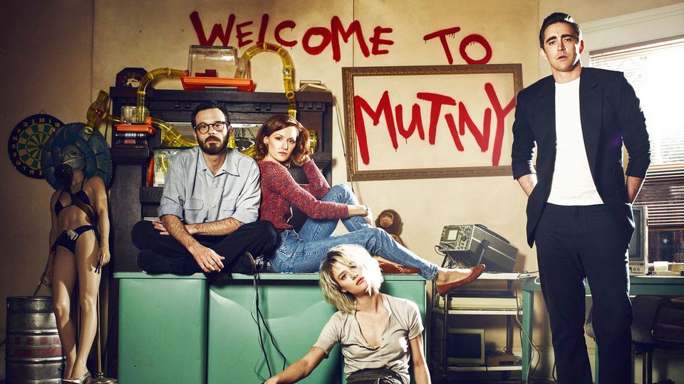 The cast of 'Halt and Catch Fire' in a messy room with the words 'Welcome to Mutiny' spray painted behind them. 