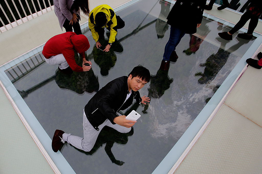 Tourists take pictures with their iphone on the glass-floor