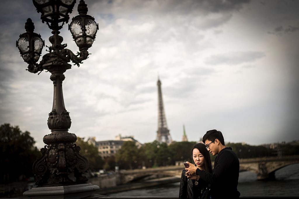 A young couple looks at a smartphone in front of the Eiffel Tower