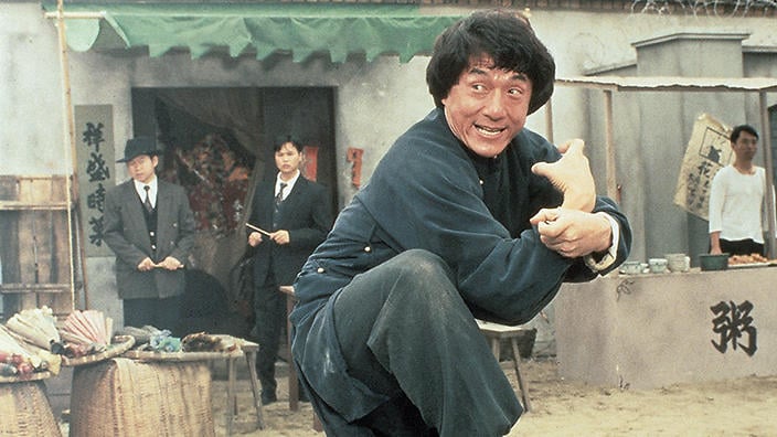 Jackie Chan in a blue jumpsuit, with his fists out, ready to fight