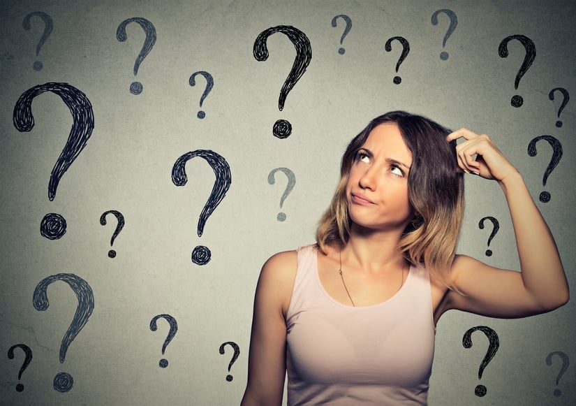 Thinking young woman looking up at many question marks