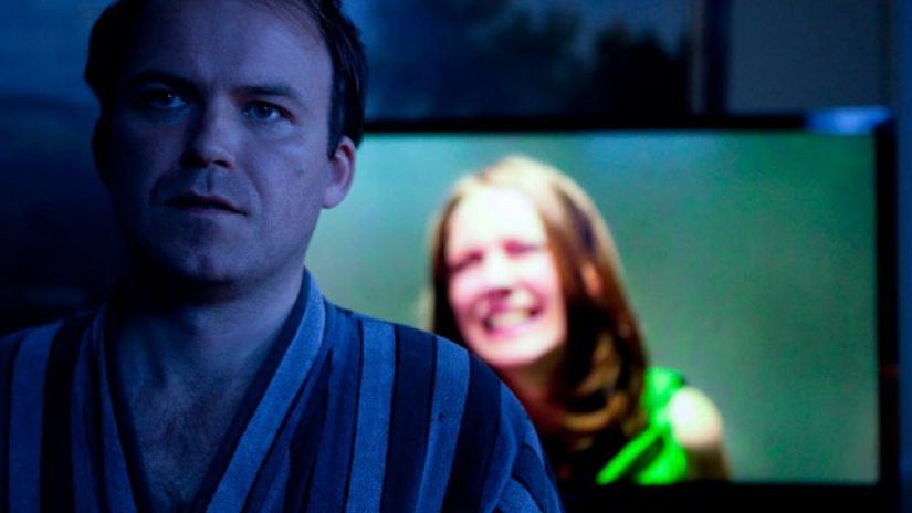 Prime Minister Callow (Rory Kinnear) sits in front of a screen displaying kidnapped Princess Susannah (Lydia Wilson) in a scene from the 'Black Mirror' episode "The National Anthem"