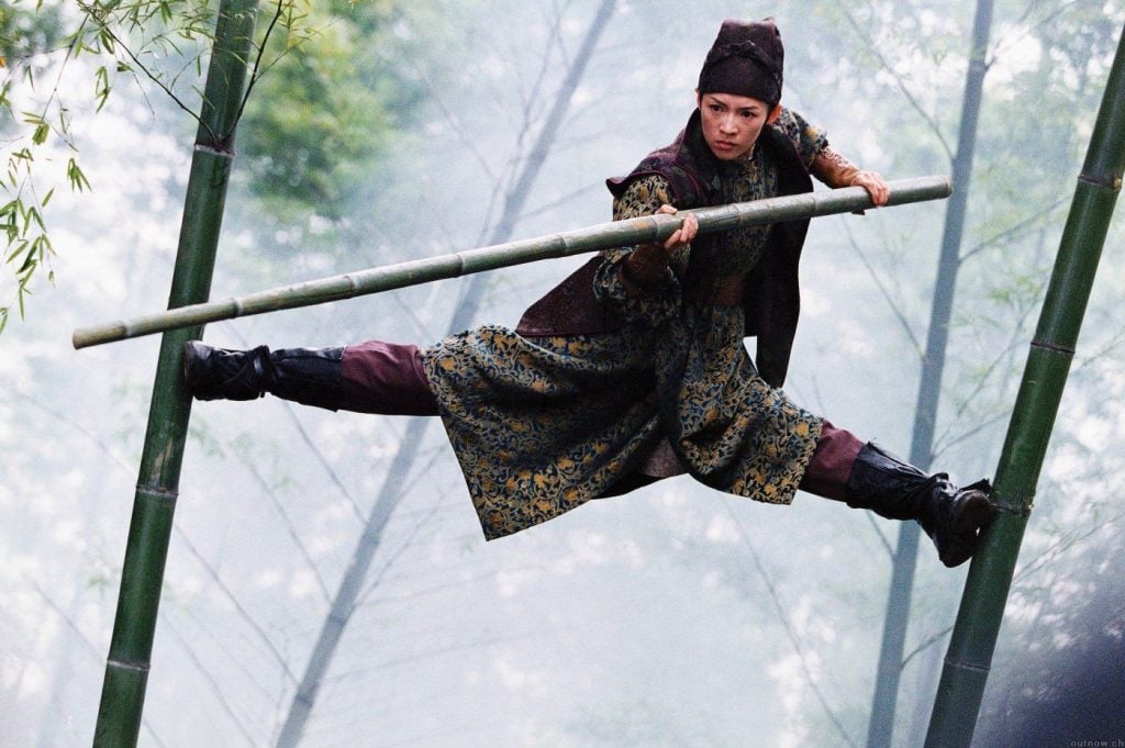 A woman balancing on two large bamboo stalks, holding a pole out in front of her for balance