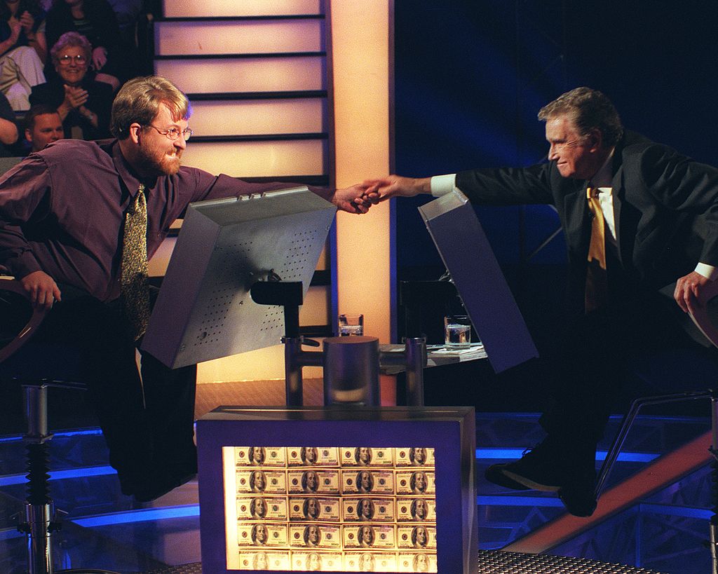 Contestant Doug Van Gundy shakes the hand of host Regis Philbin as they sit in front of their monitors on Who Wants to Be a Millionaire