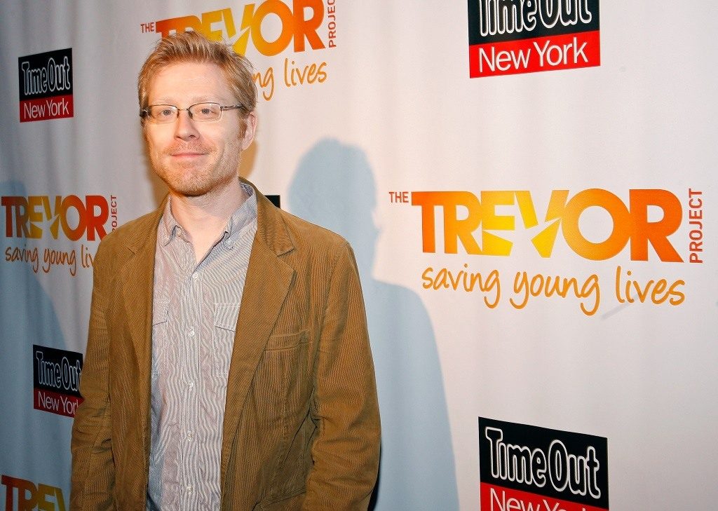 Actor Anthony Rapp on the red carpet, wearing a brown jacket and smiling for the camera