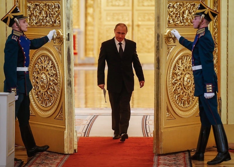 Vladimir Putin walks through an ornate gold door with guards on either side of him