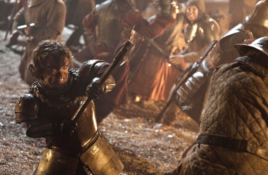 Tyrion yelling angrily, dressed in armor and wielding an ax in the middle of a raging battlefield