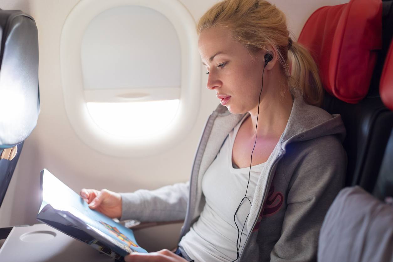 Woman reading magazine and listening to music on an airplane
