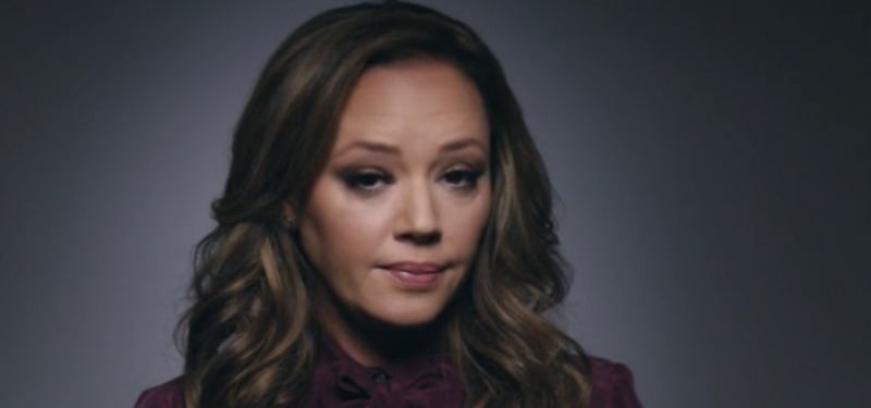 Leah Remini looks directly at the camera seriously in front of a dark background