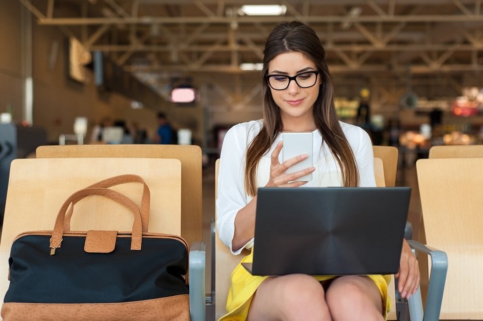 Young female passenger on smart phone and laptop sitting in terminal