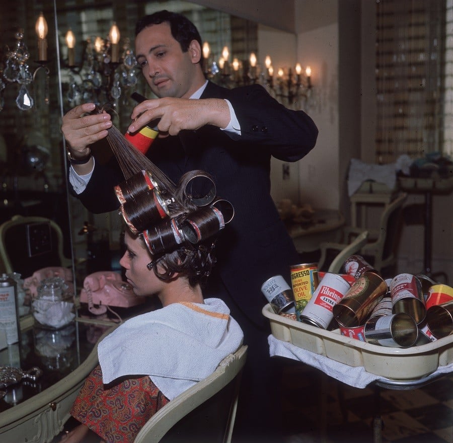A hairdresser styling a woman's hair using beer cans as curlers