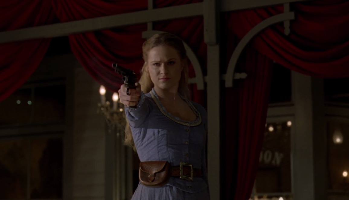 Dolores aiming a gun in front of a western backdrop