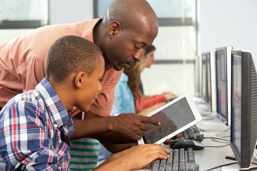 Teacher helps boy to use digital tablet